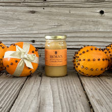 Load image into Gallery viewer, Jar of Bjorn's honey with decorative pomanders (citrus with cloves) on a wooden surface