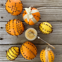 Load image into Gallery viewer, Decorative oranges with cloves stuck in them on a wooden surface with a open jar of Whipped Pomander Honey.